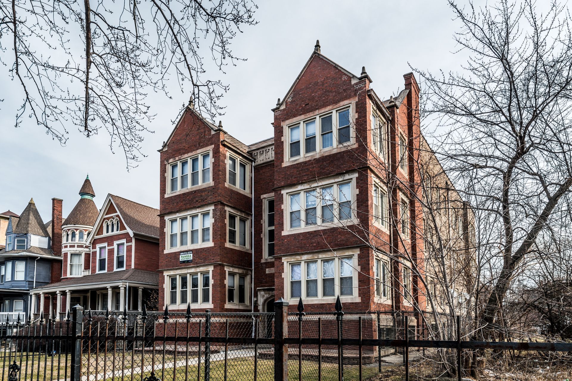 Brick apartment building with multiple windows, wrought iron fence in front.