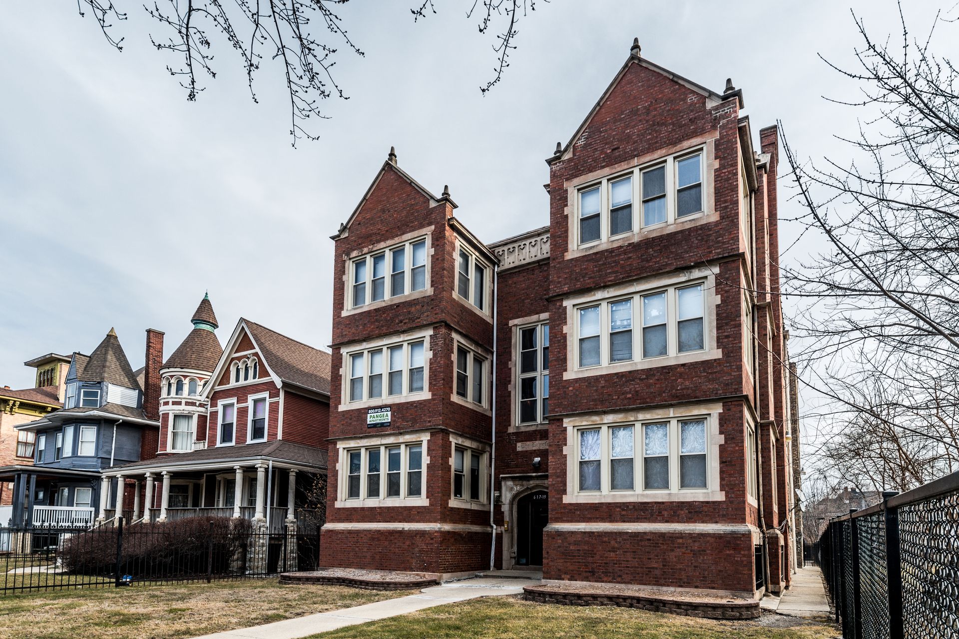 Brick apartment building with gabled roof, flanked by colorful Victorian houses.