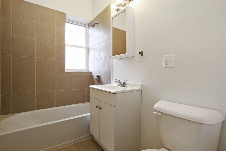 Bathroom with white fixtures, beige tile, and a window.