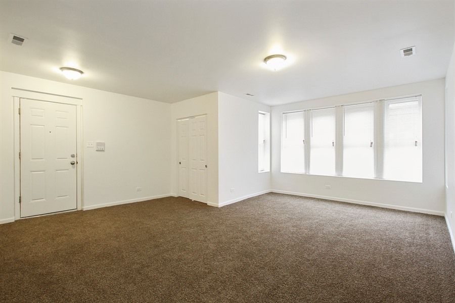 Empty room with brown carpet, white walls, two doors, and a window with blinds.