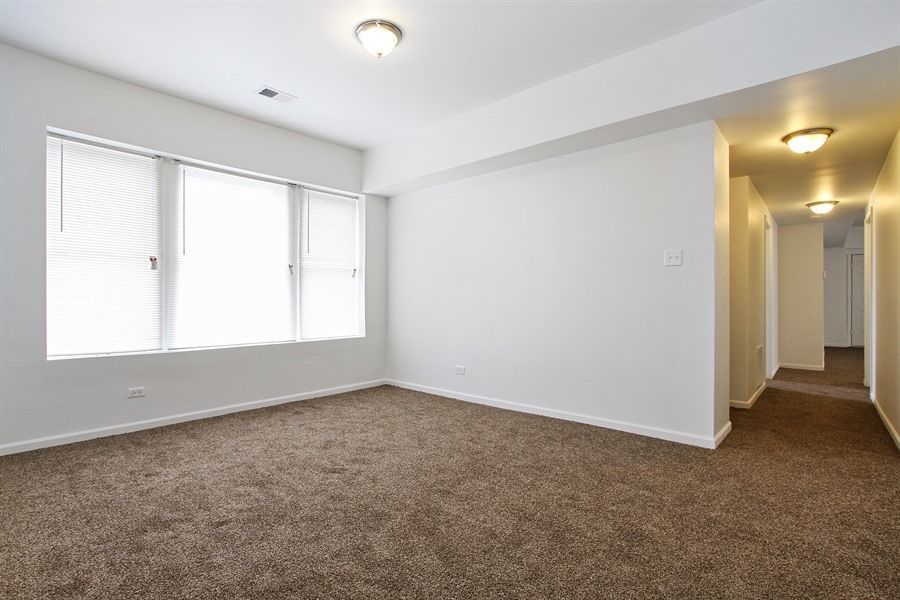 Empty room with brown carpet, white walls, and a hallway.