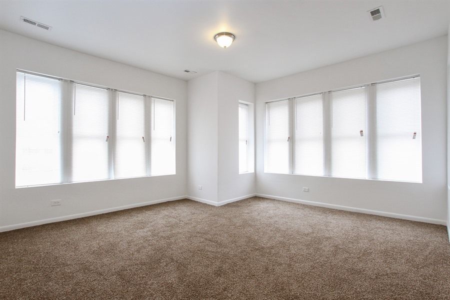 Empty room with brown carpet, white walls, and multiple windows with blinds.