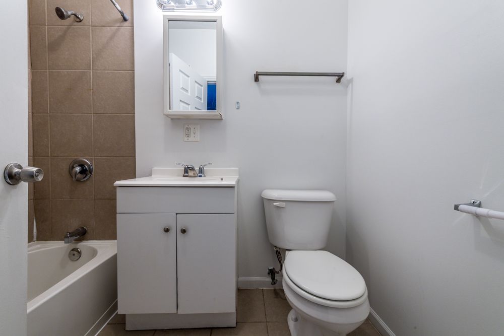 Bathroom with white walls, toilet, vanity, and a shower/tub combo.