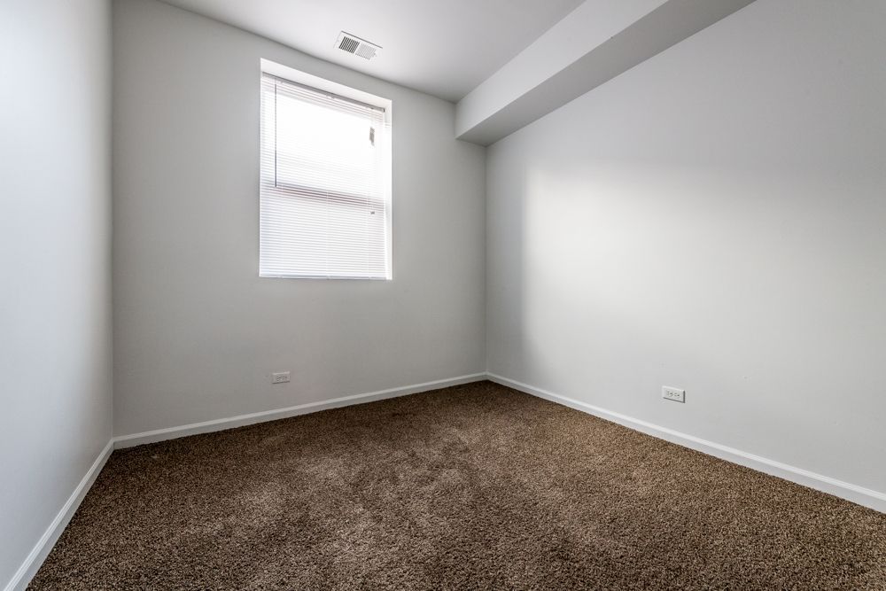Empty room with brown carpet, window with blinds, and white walls.
