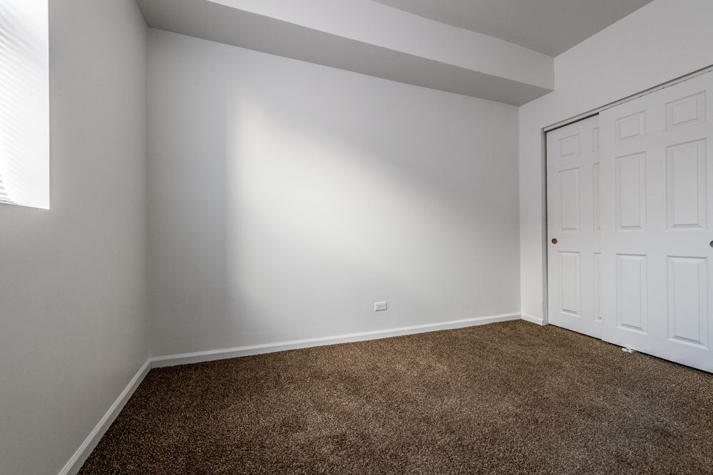 Empty room with white walls, brown carpet, and closet doors. Natural light from a window.