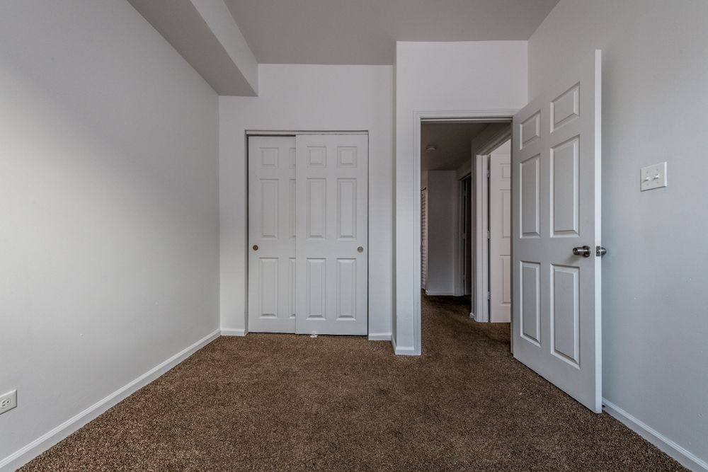 Empty room with white walls, closet, open door, and brown carpet.
