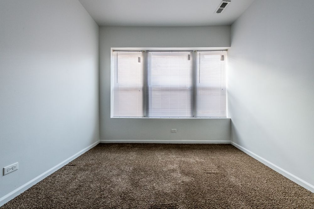 Empty room with brown carpet, white walls, and a window with blinds.