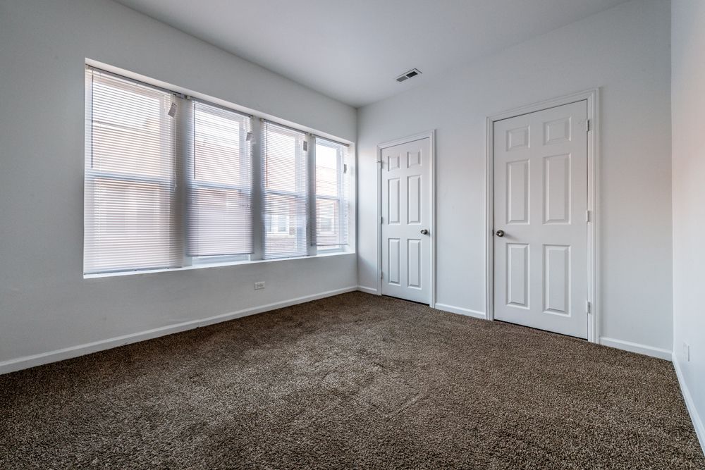 Empty room with brown carpet, white walls, two doors, and a window with blinds.