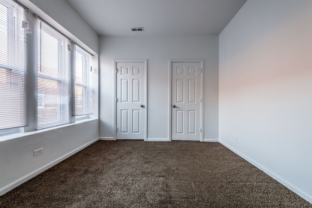 Empty room with two doors and a window, brown carpet, white walls.