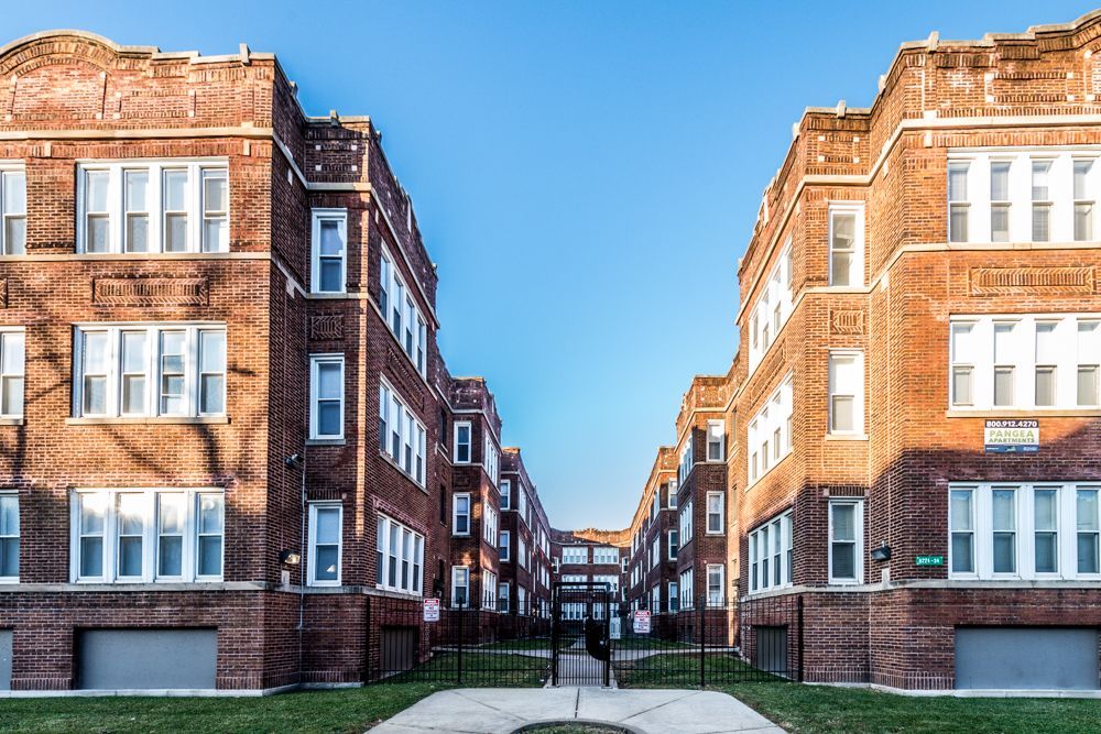 Two brick apartment buildings face each other, forming a courtyard. Blue sky overhead.