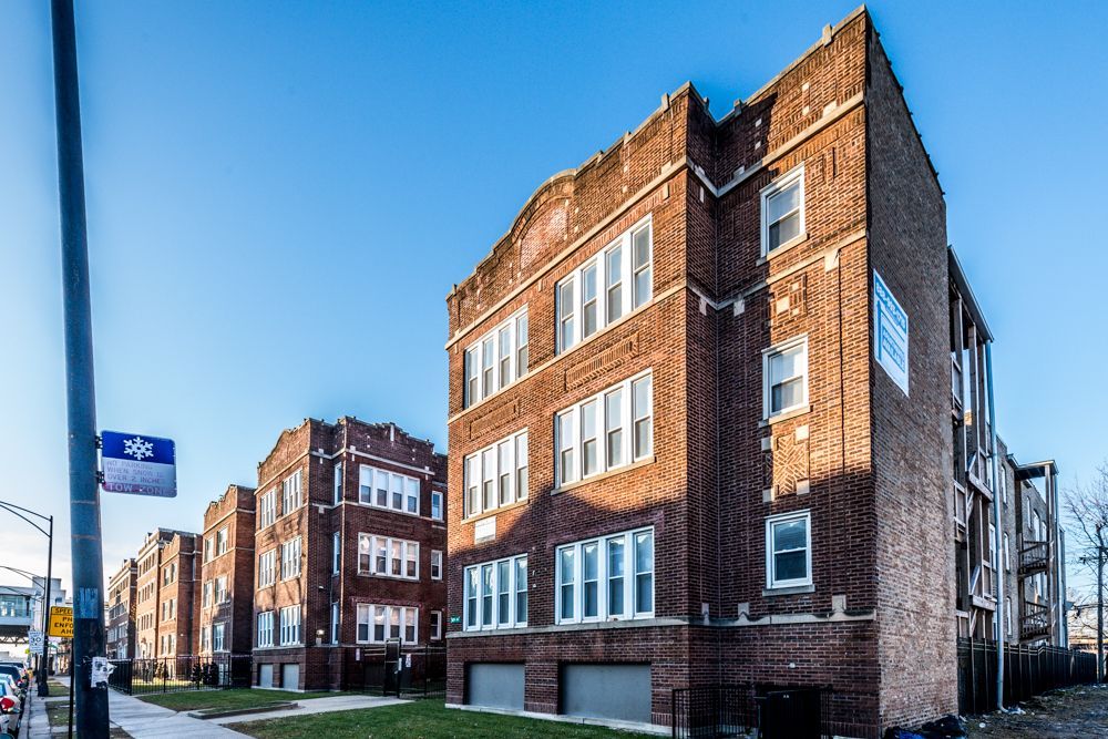 Brick apartment buildings on a sunny city street with blue sky.