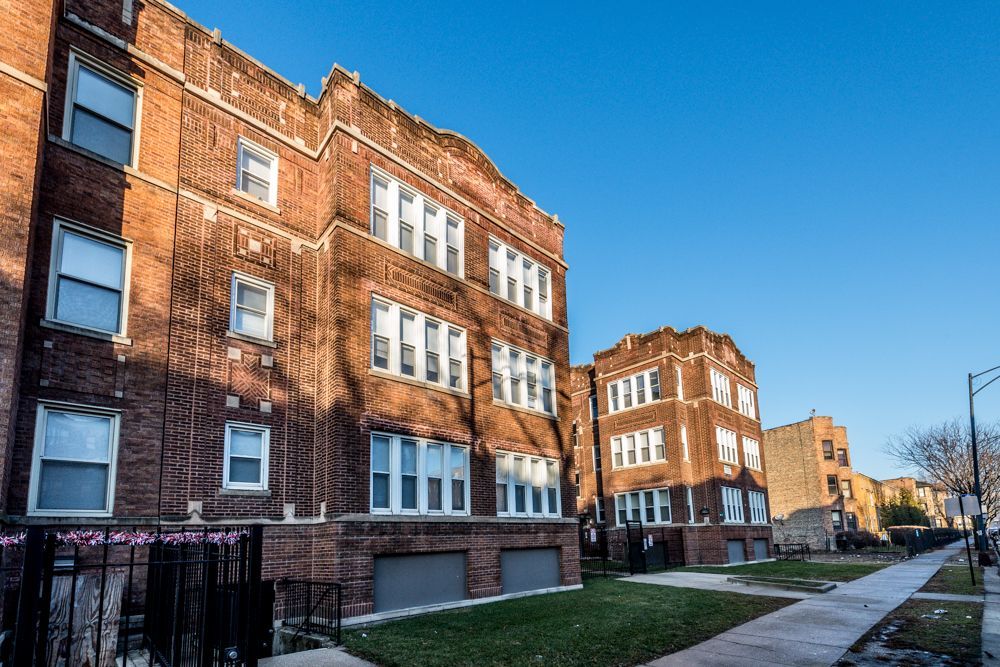 Brick apartment buildings on a city street, blue sky above.