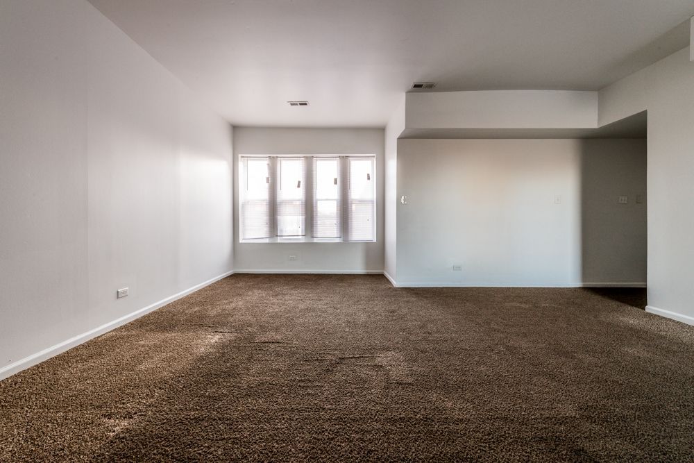 Empty room with brown carpet, white walls, and a window.