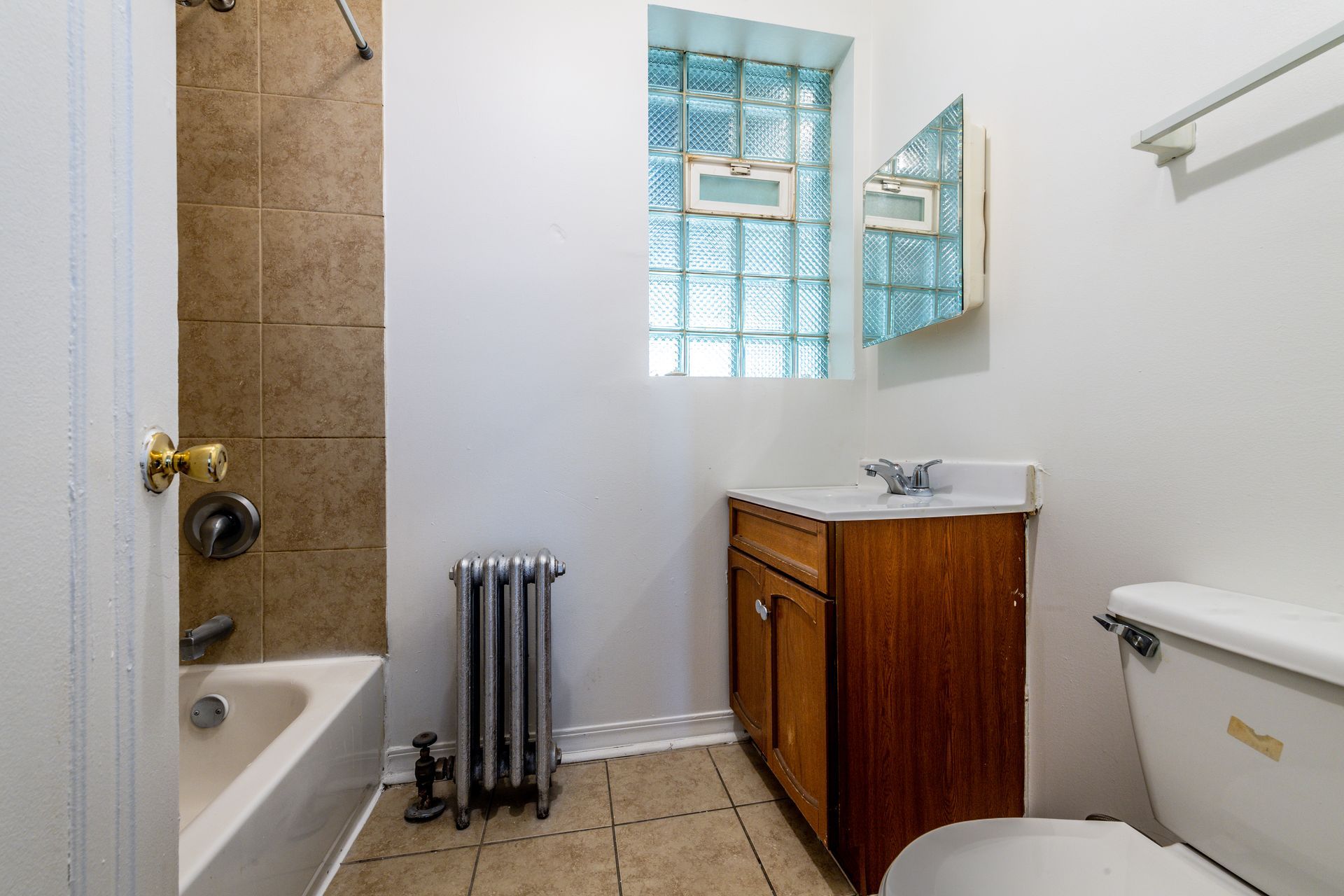 Bathroom with a tub/shower, sink, toilet, radiator, and a glass block window.