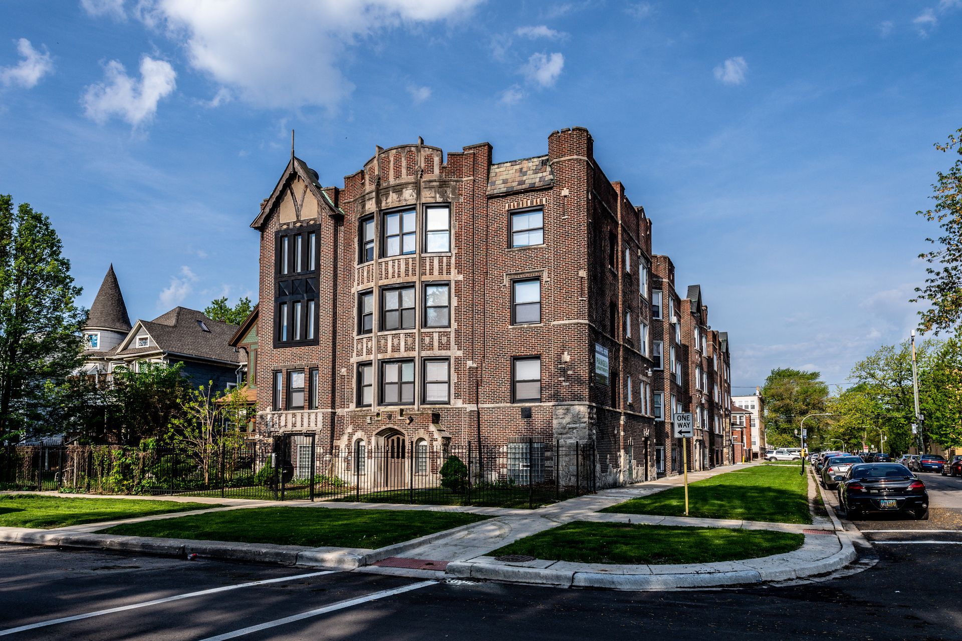 Brick apartment building on a corner lot, with dark trim and a Gothic-style facade under a blue sky.