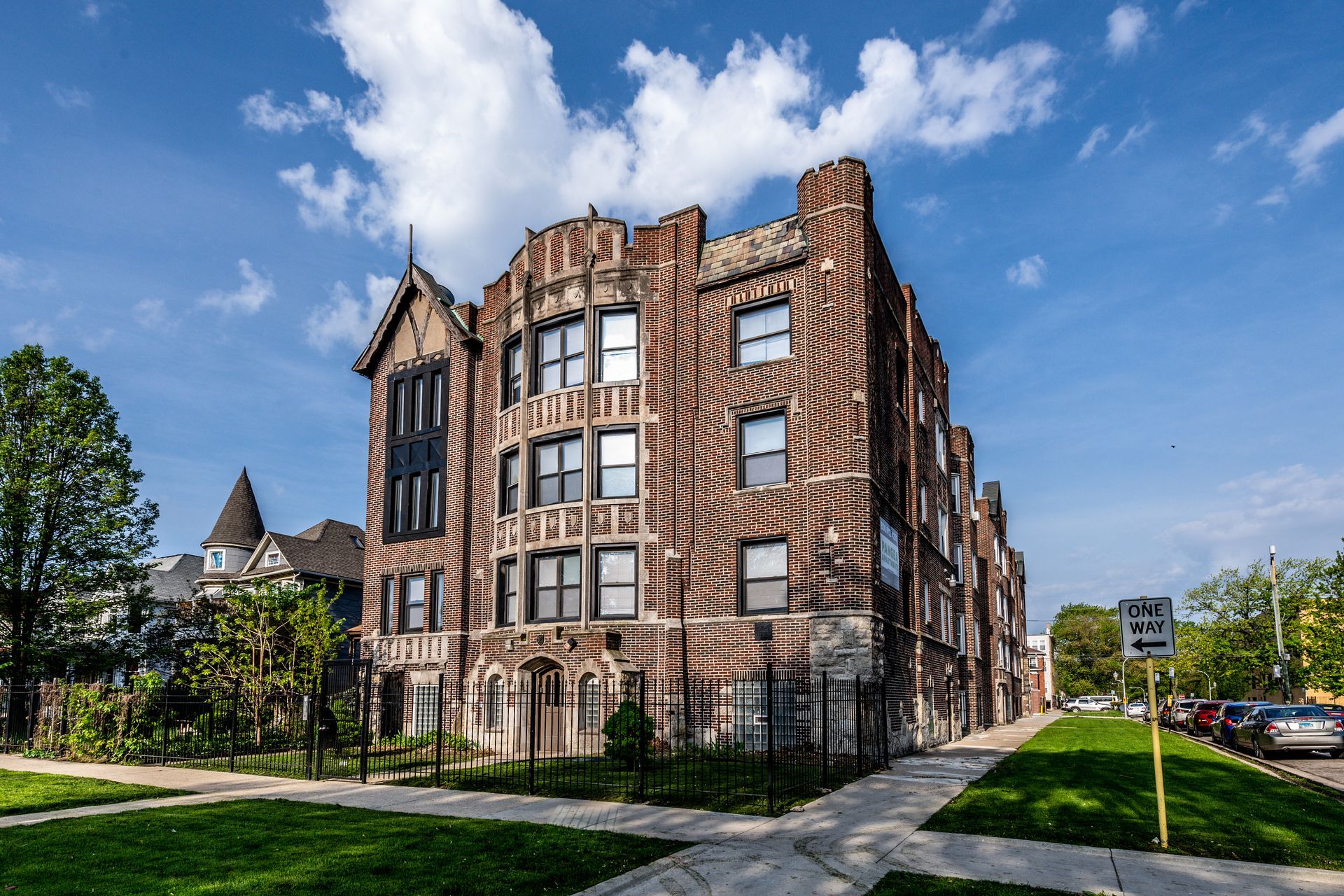 Multi-story brick apartment building on a sunny day; lawn and sidewalk in foreground.