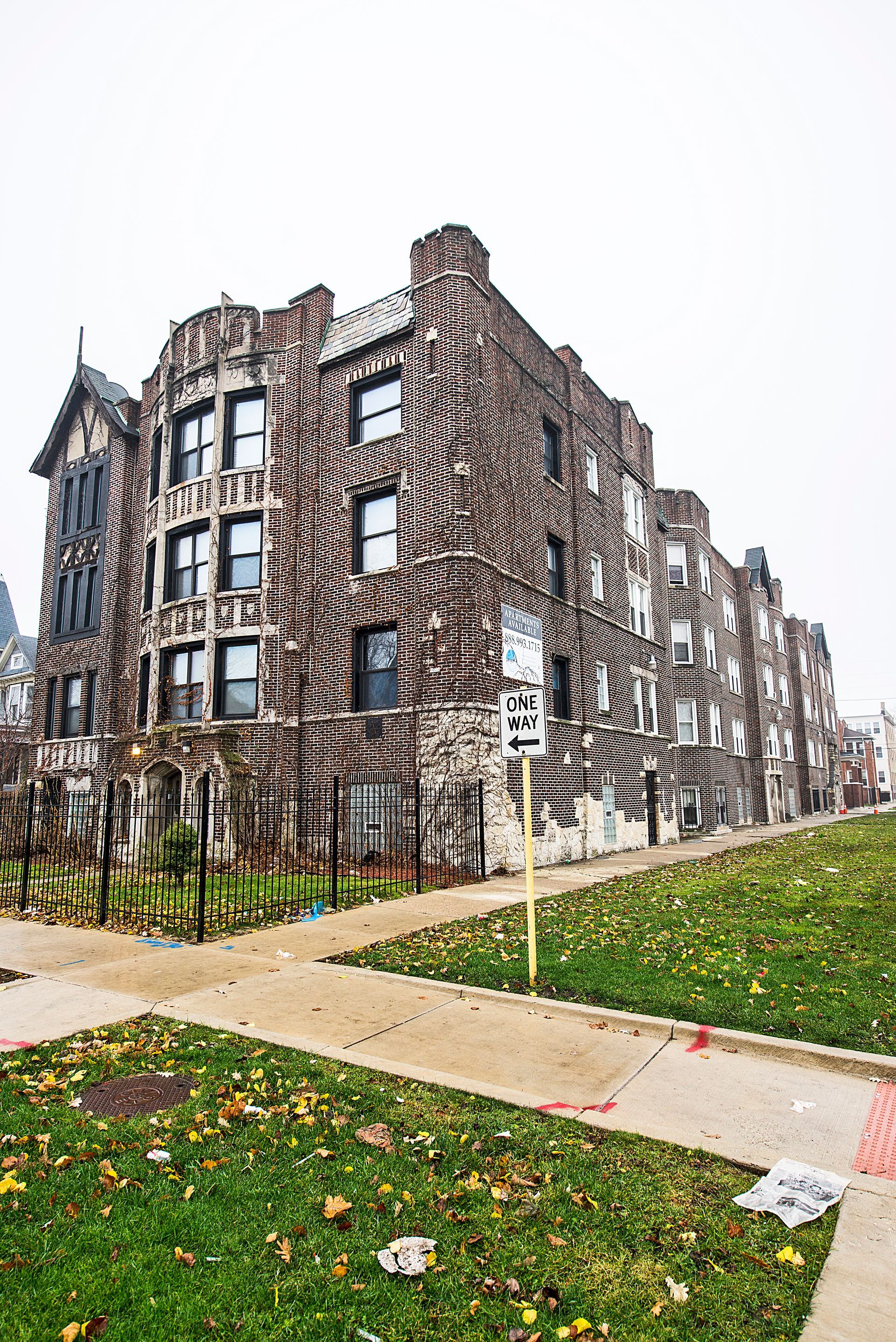 Brick apartment building on a grassy hill, with a street sign. Overcast sky.