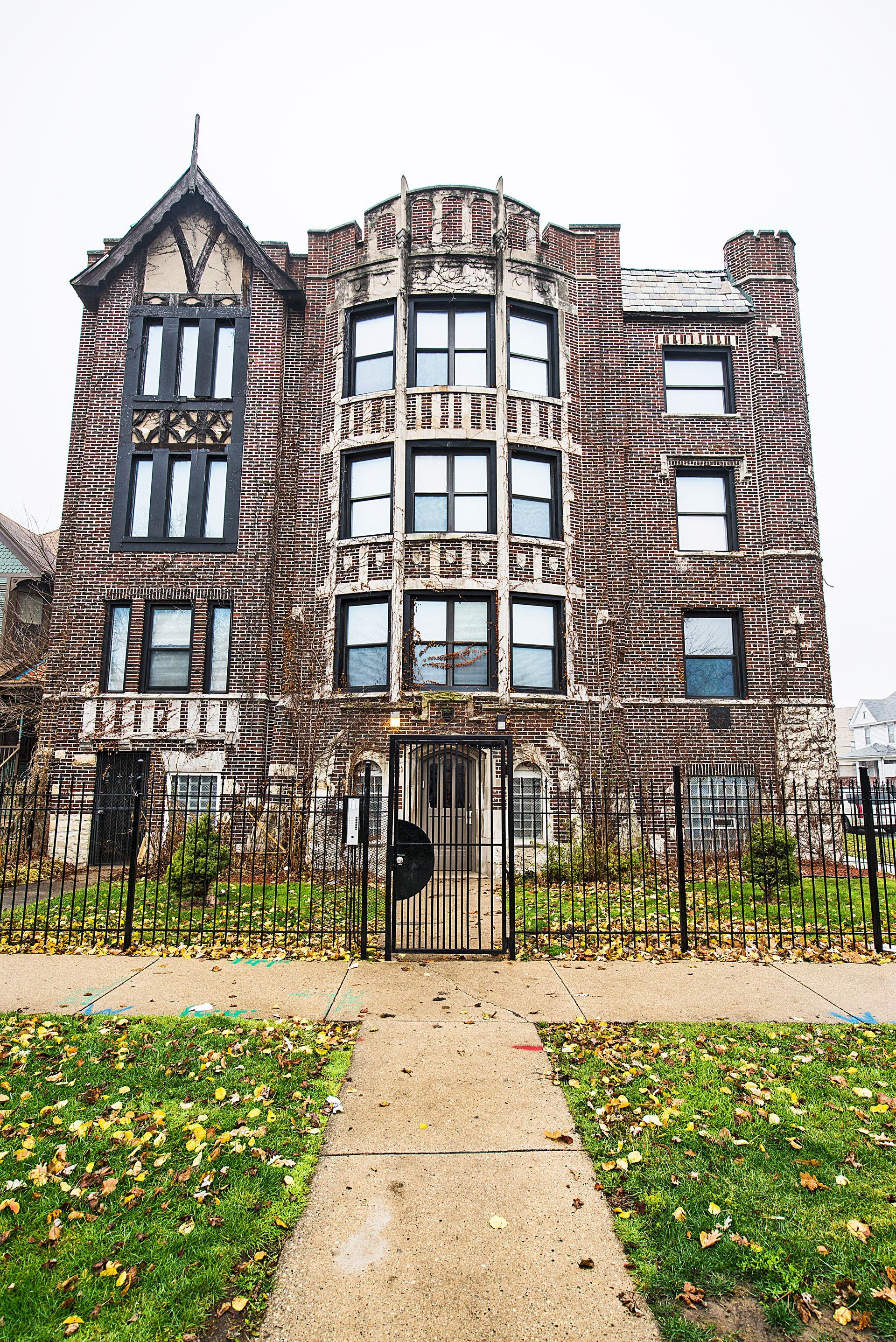 Brick building with a gated entry, windows, and decorative detailing; a walkway and grass in the foreground.