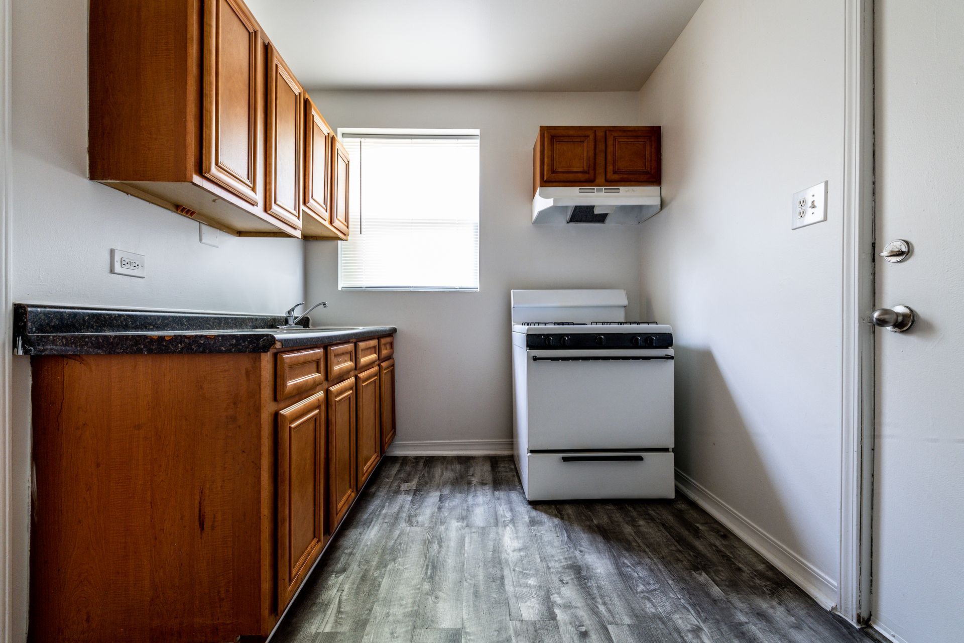 Kitchen with wooden cabinets, white stove, and window. Gray flooring.