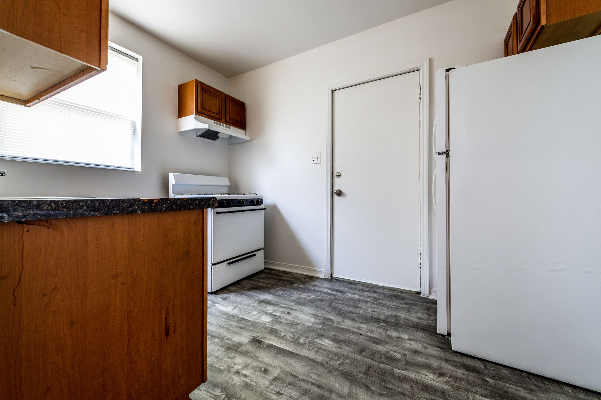 Kitchen with brown cabinets, white appliances, and gray flooring.