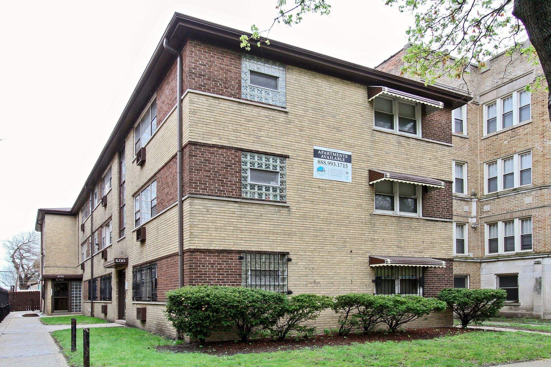Multi-story brick apartment building with beige facade, green lawn.