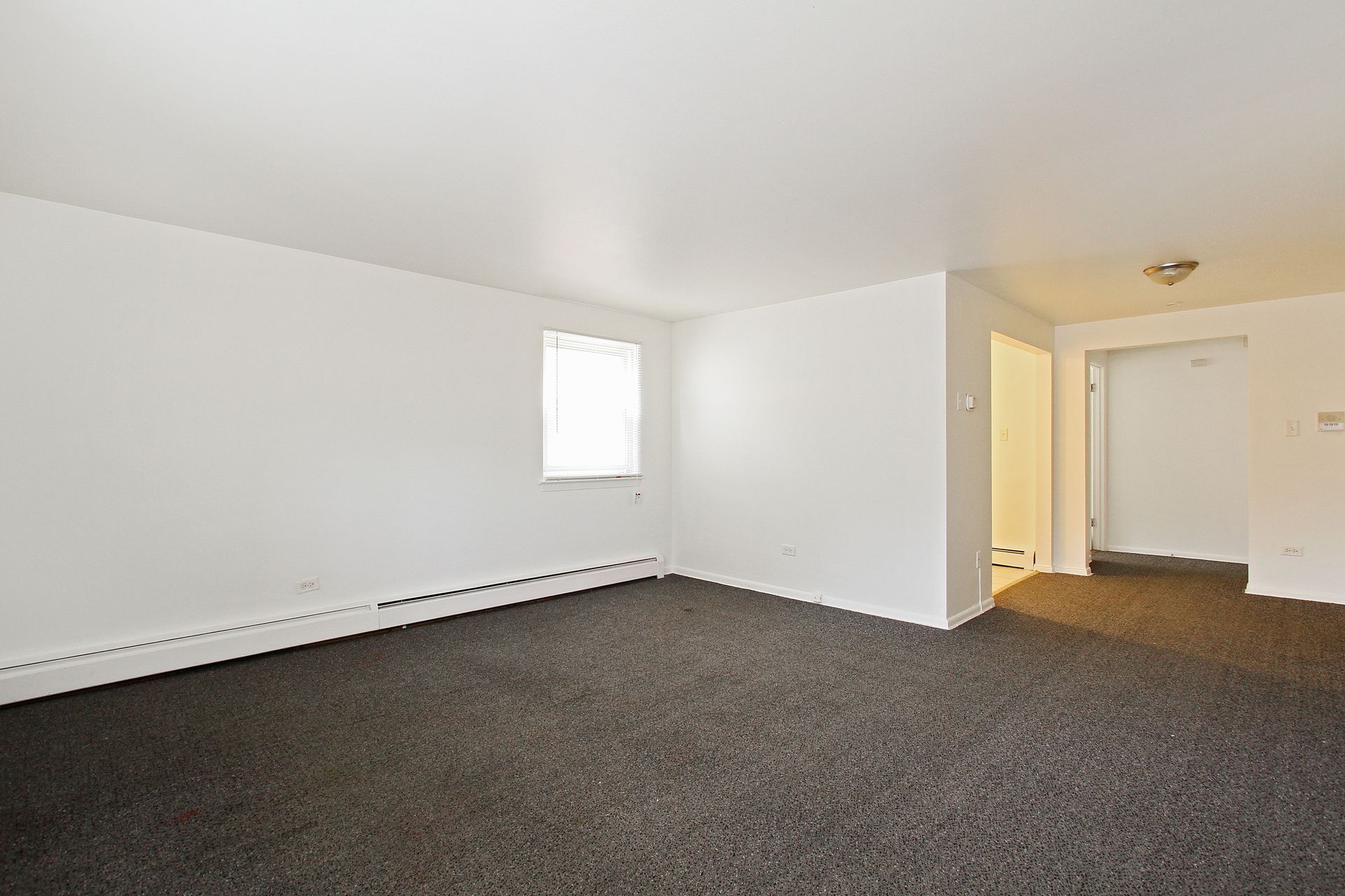 Empty living room with gray carpet, white walls, and a doorway.