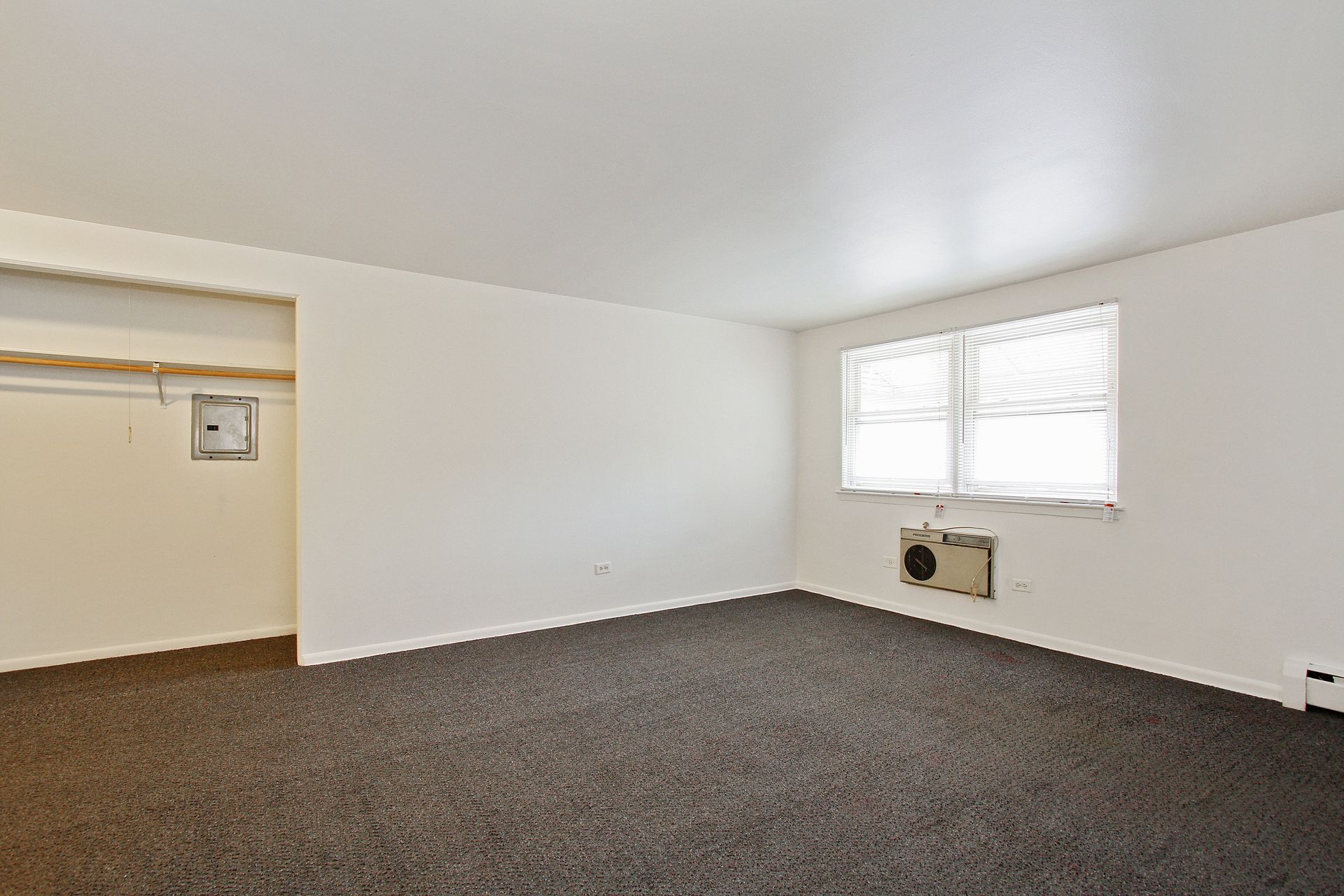 Empty room with gray carpet, white walls, closet, and window with air conditioner.