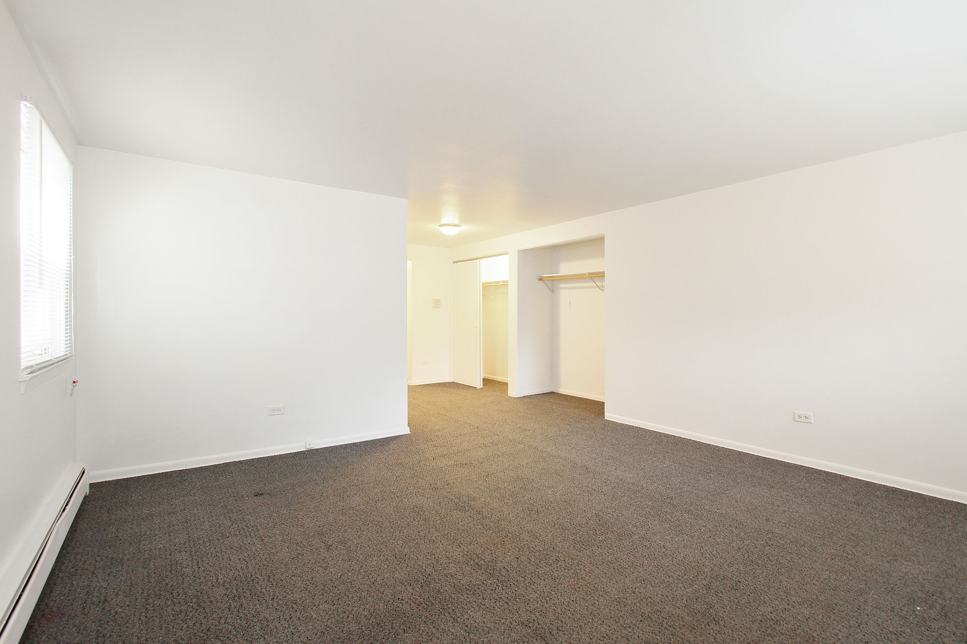 Empty, rectangular room with gray carpet and white walls, closet and doorway visible.