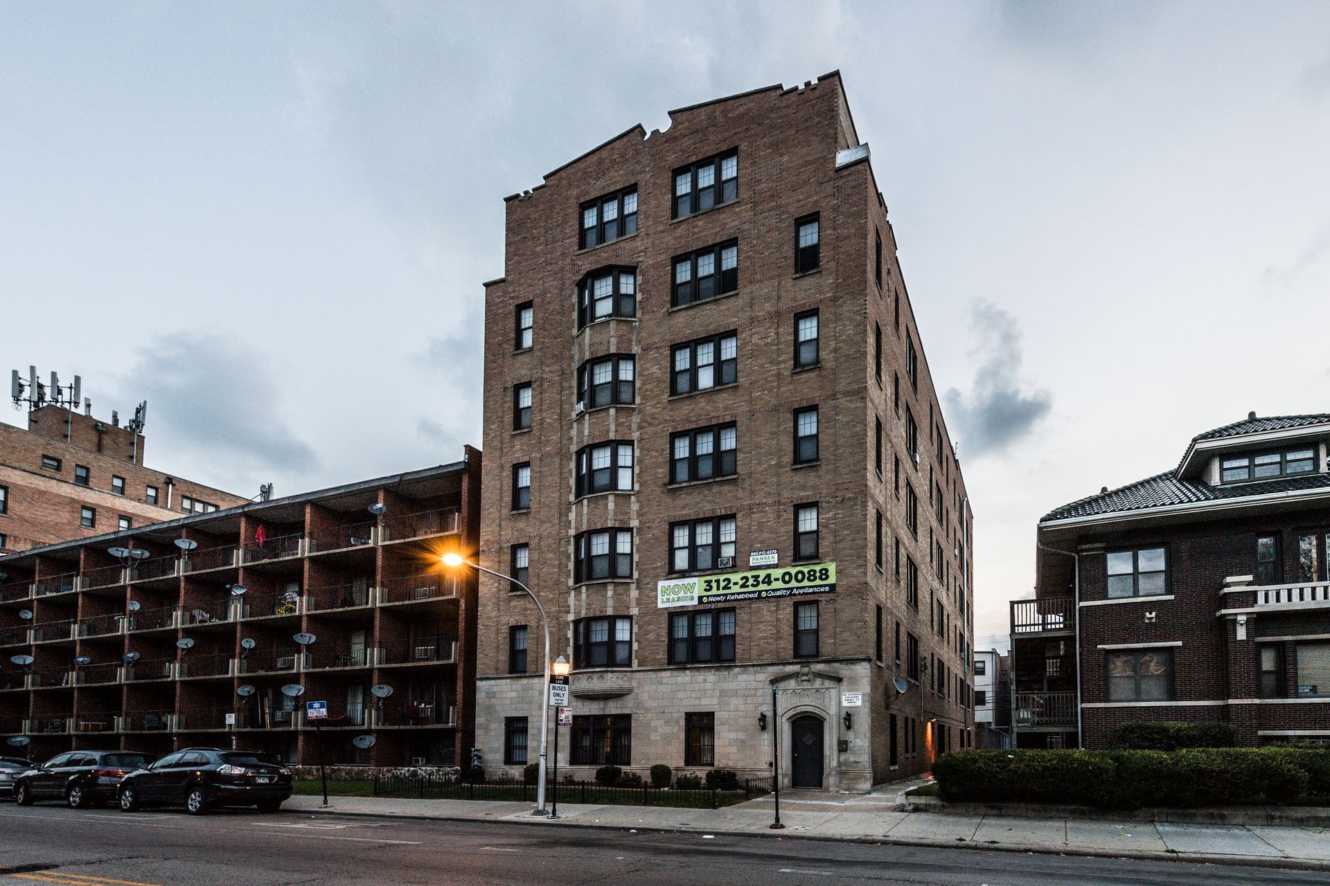 Brick apartment building on a city street; overcast sky; cars parked nearby.
