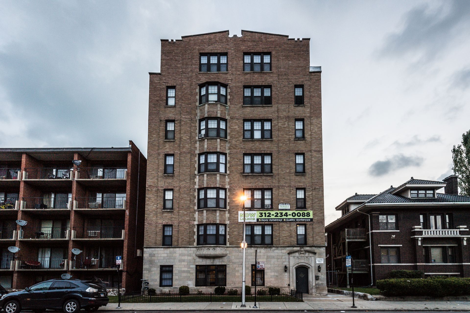 Brick apartment building with cream-colored accents, standing between two other buildings under a cloudy sky.
