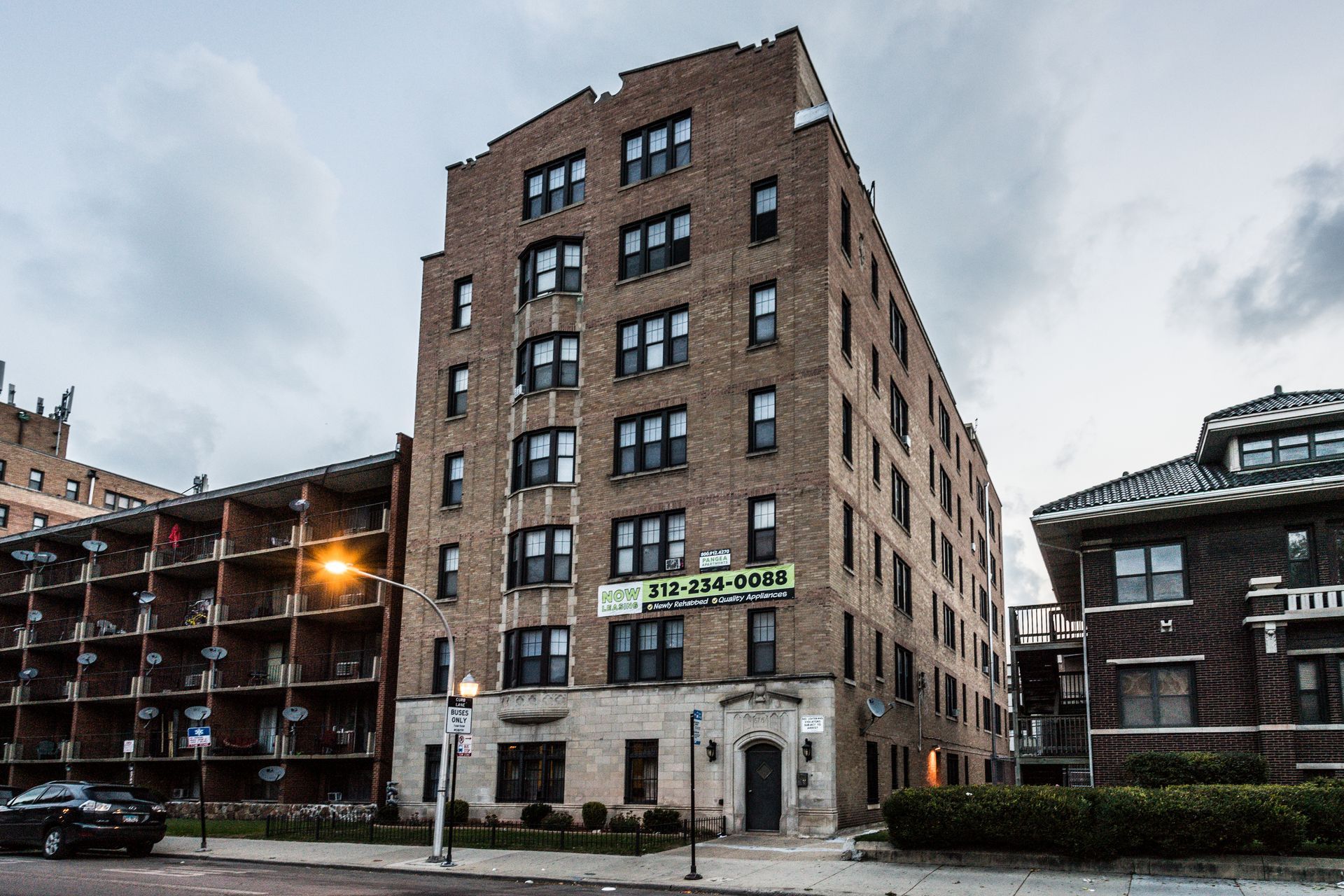 Apartment building with brick exterior and several windows. A sign displays a phone number.