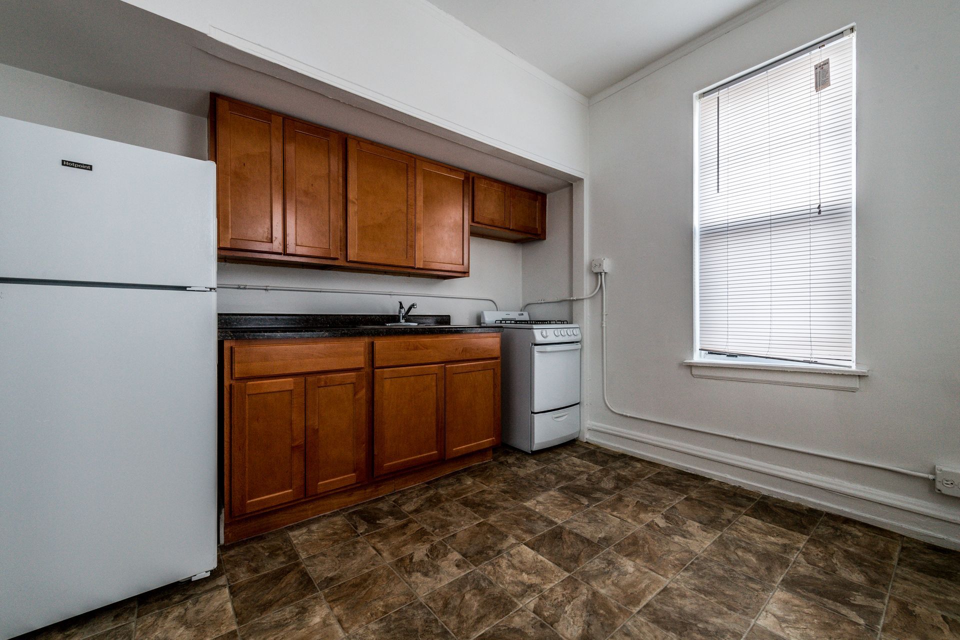 Kitchen with brown cabinets, white appliances, and a window with blinds.