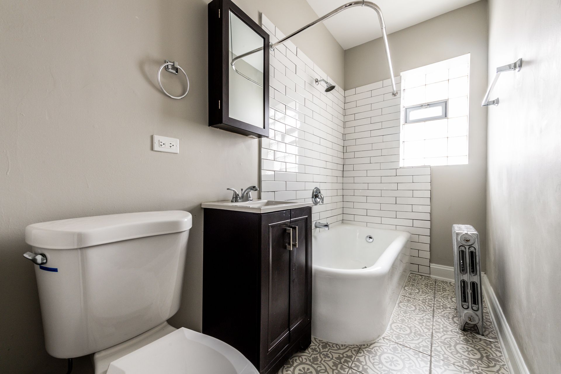 Bathroom with white toilet, vanity, tub, patterned floor, and white tile wall.