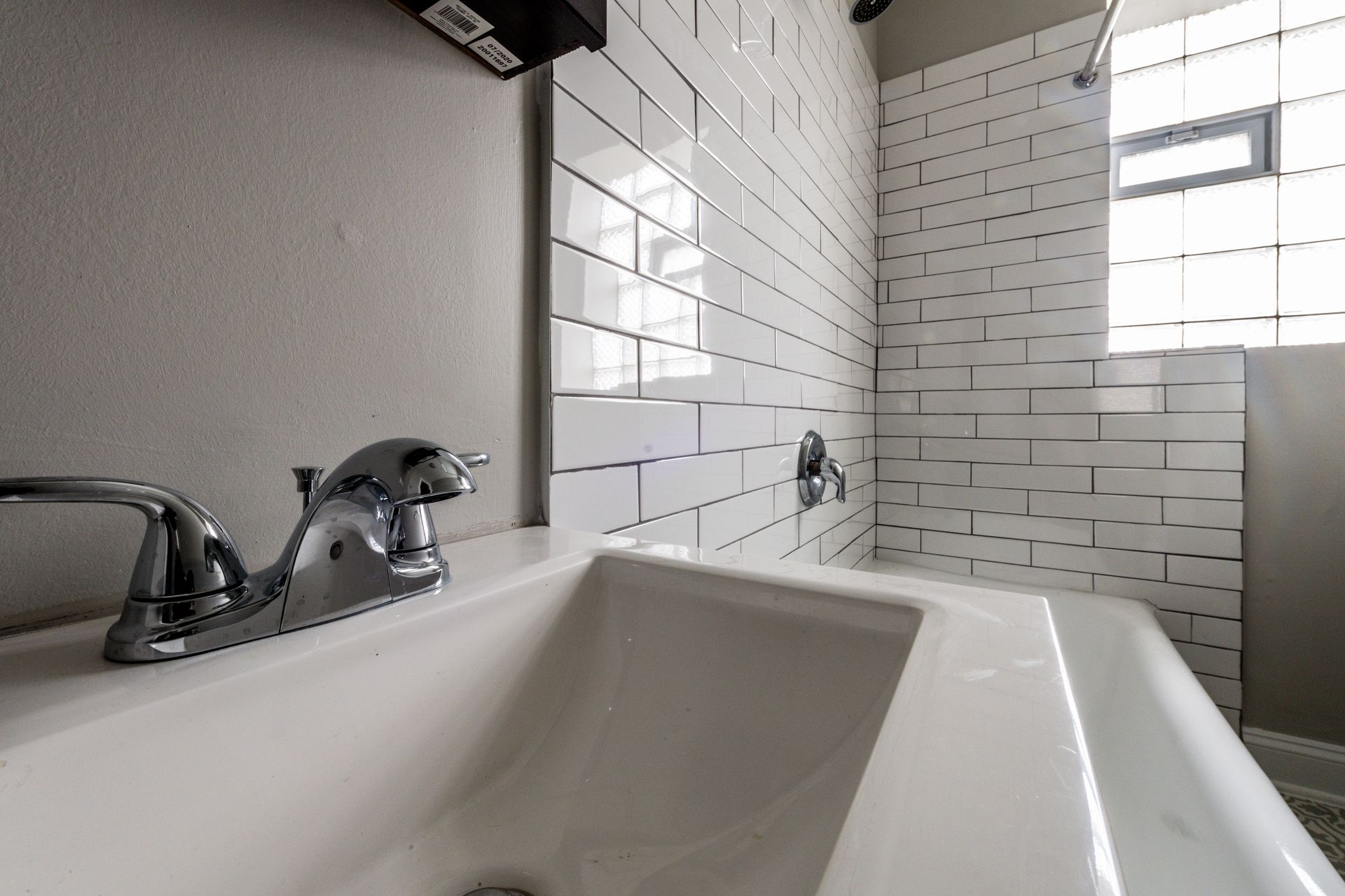 White bathroom sink and faucet with subway tile shower in the background.