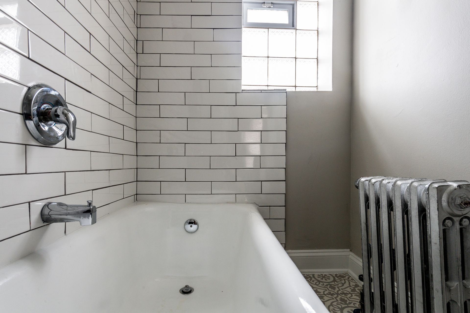 Bathroom with white subway tile, a bathtub, and a radiator.