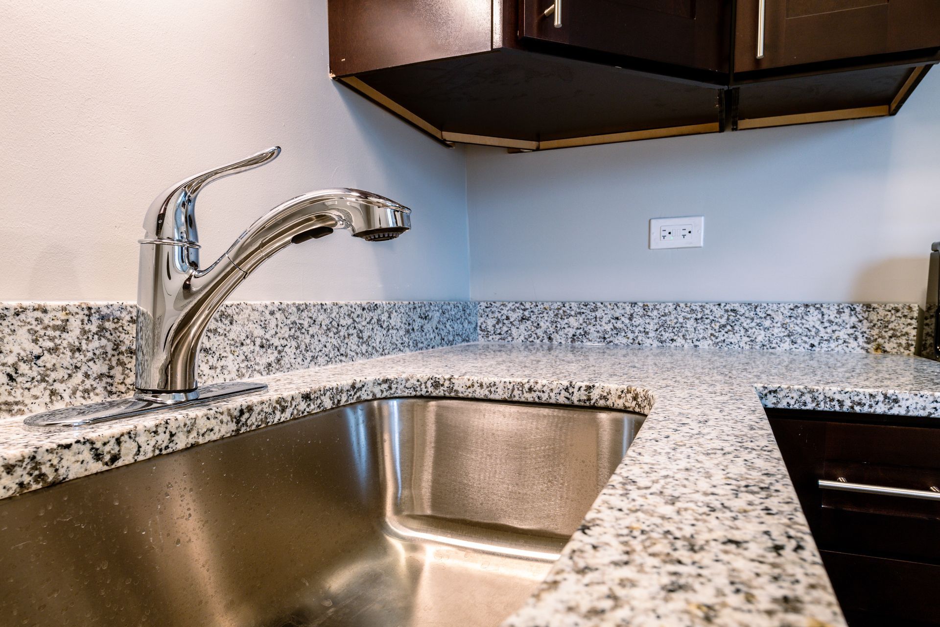 Stainless steel sink with chrome faucet, granite countertop, and dark brown cabinets.