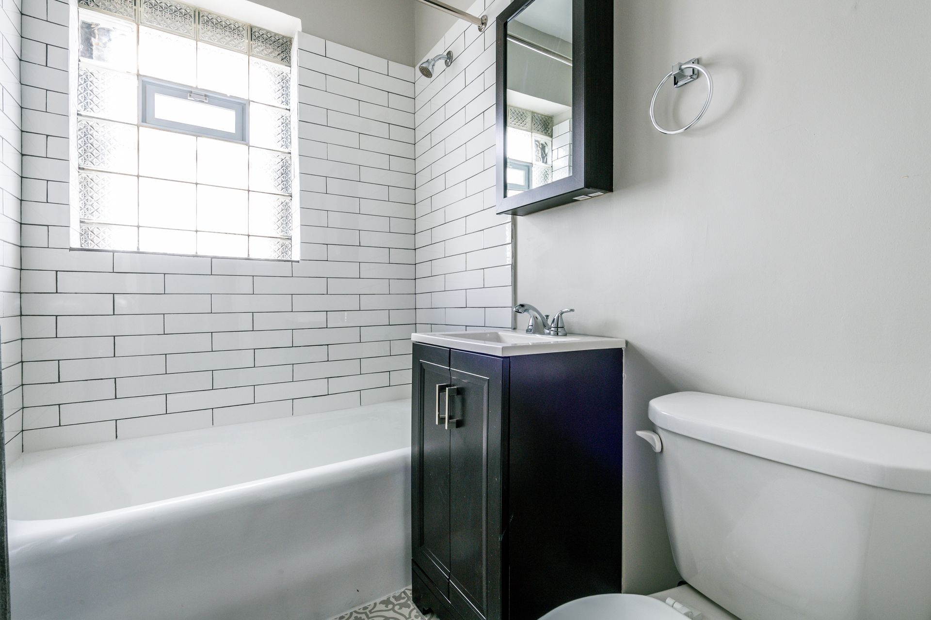 Small white bathroom with a tub, toilet, and dark vanity. White subway tile on the wall.