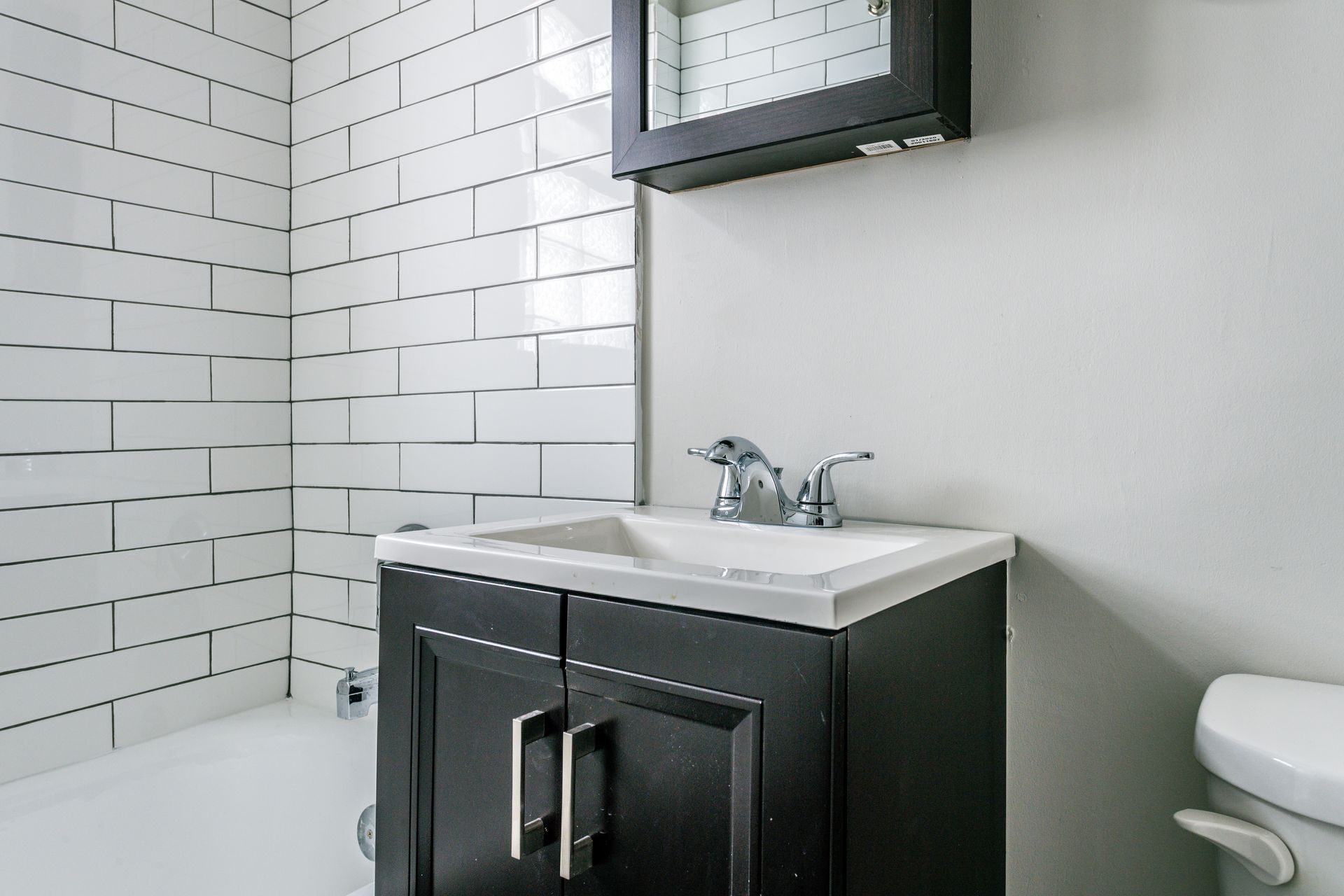 Bathroom with white subway tile, dark vanity, sink, faucet, and medicine cabinet.