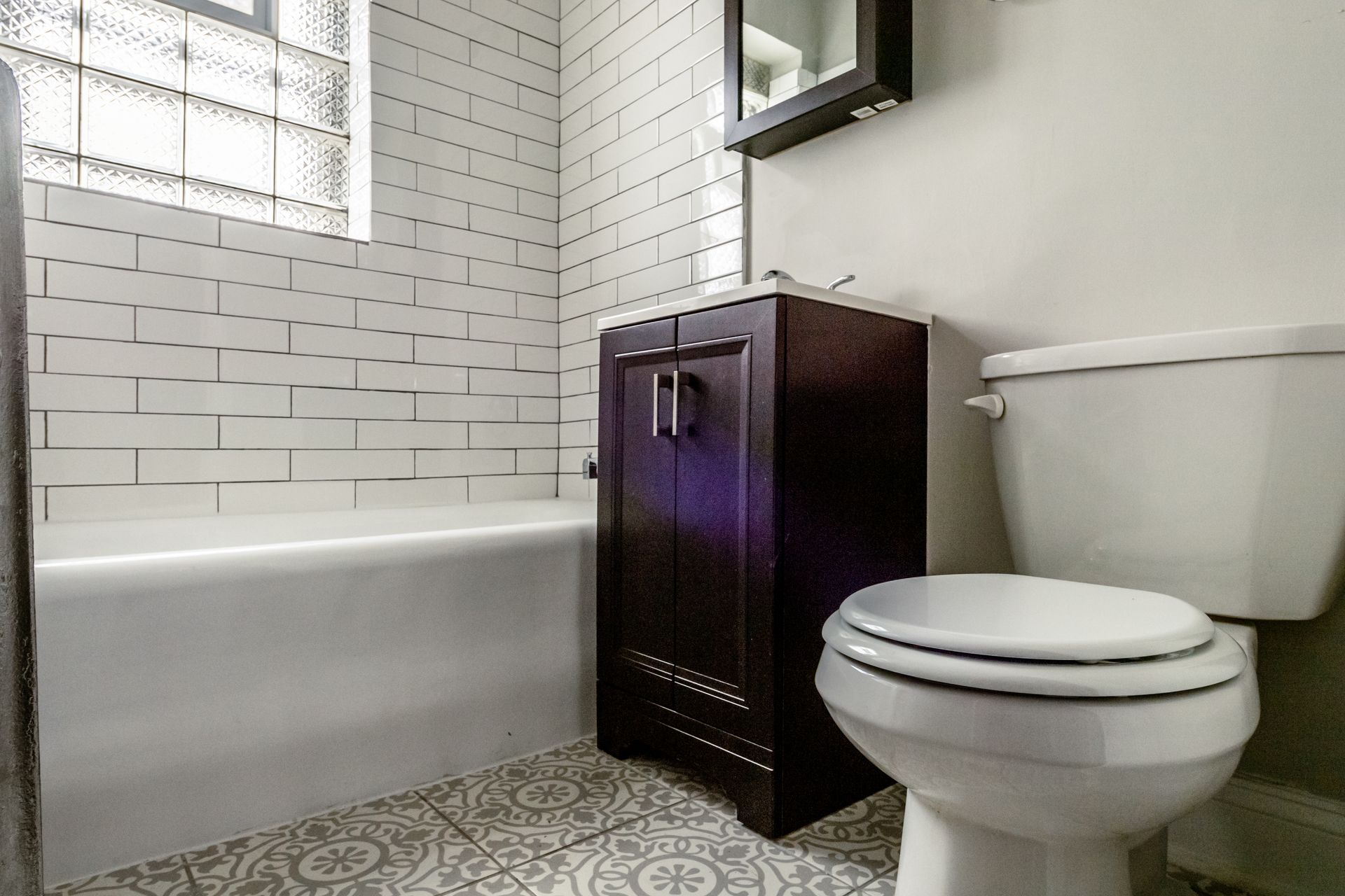 Bathroom with a white bathtub, dark wood vanity, and white toilet. White subway tile on wall.