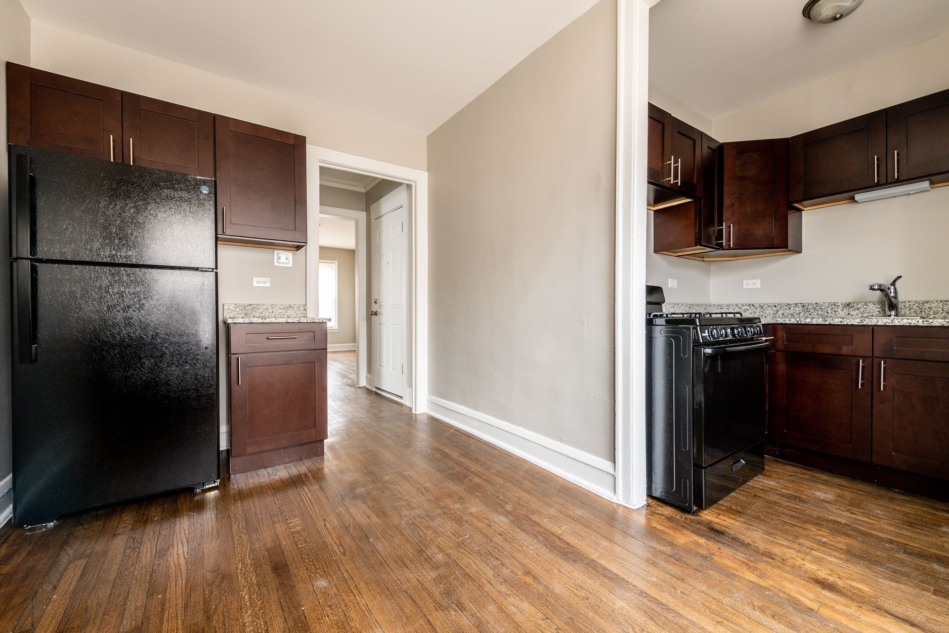 Kitchen with dark cabinets, black appliances, granite countertops, and hardwood floors.