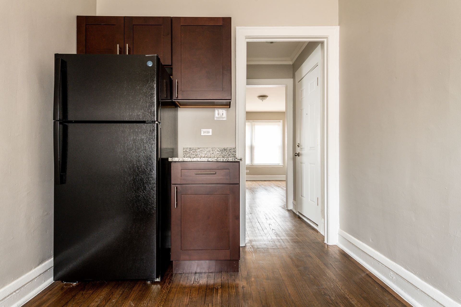 Kitchen with dark brown cabinets, black refrigerator, and doorway to a hallway.