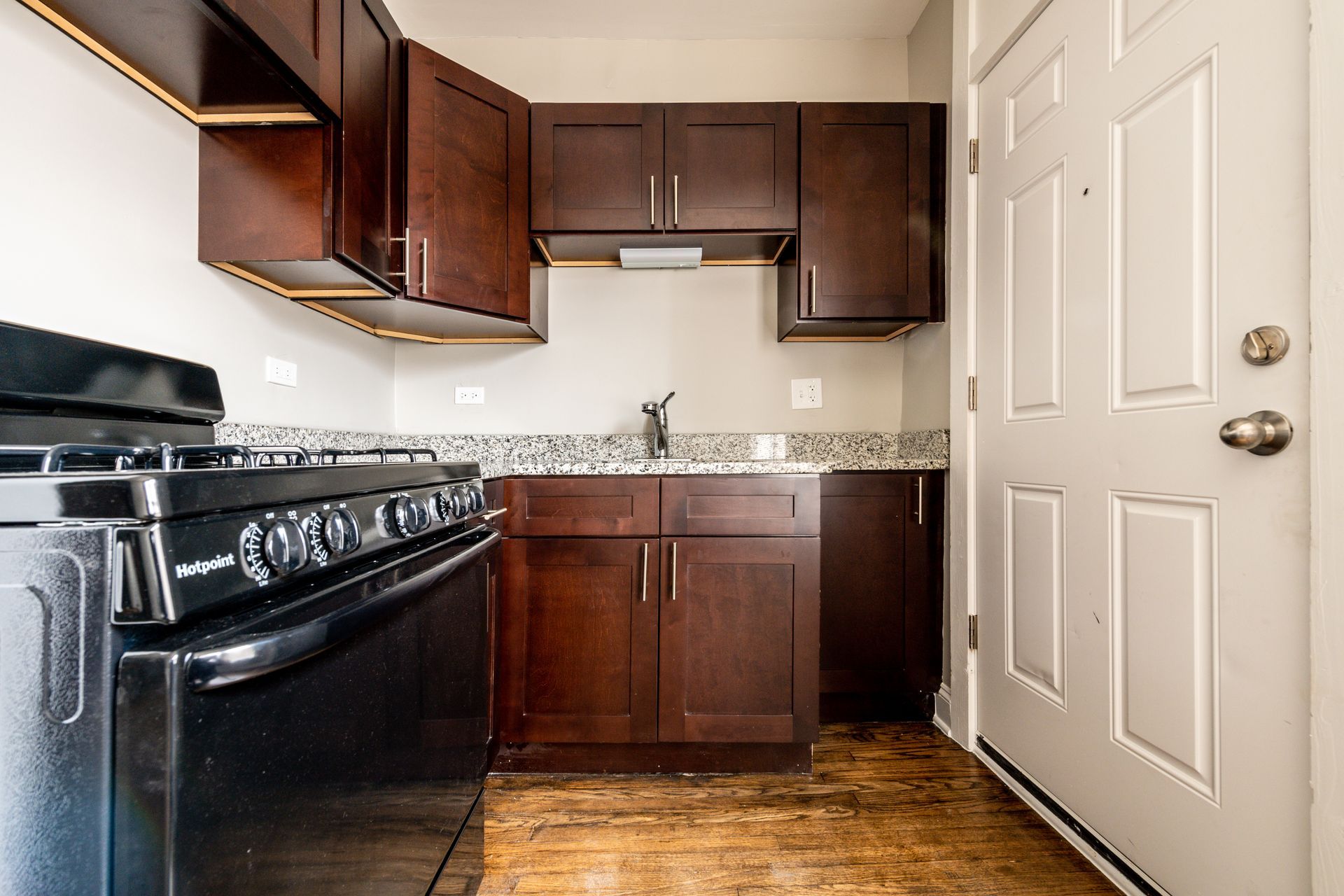 Small kitchen with dark cabinets, black stove, granite countertop, and white door.