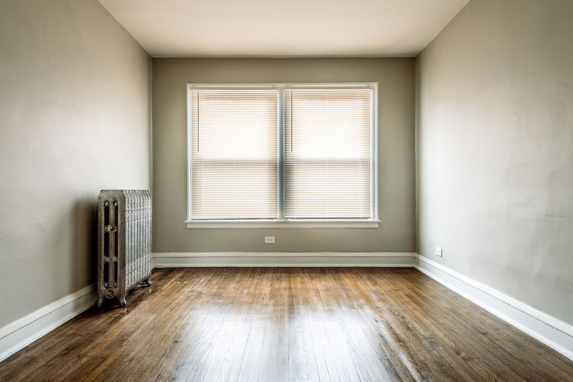 Empty room with hardwood floors, a window with blinds, and a radiator.