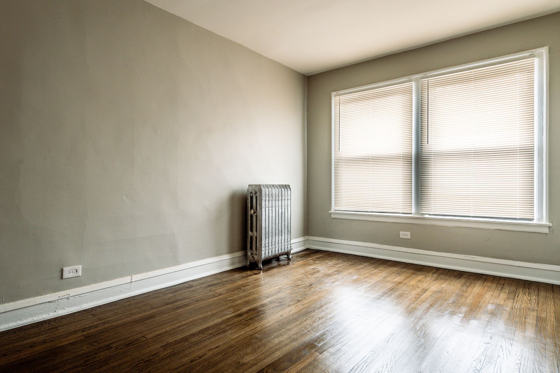 Empty room with wood floor, window with blinds, and radiator.