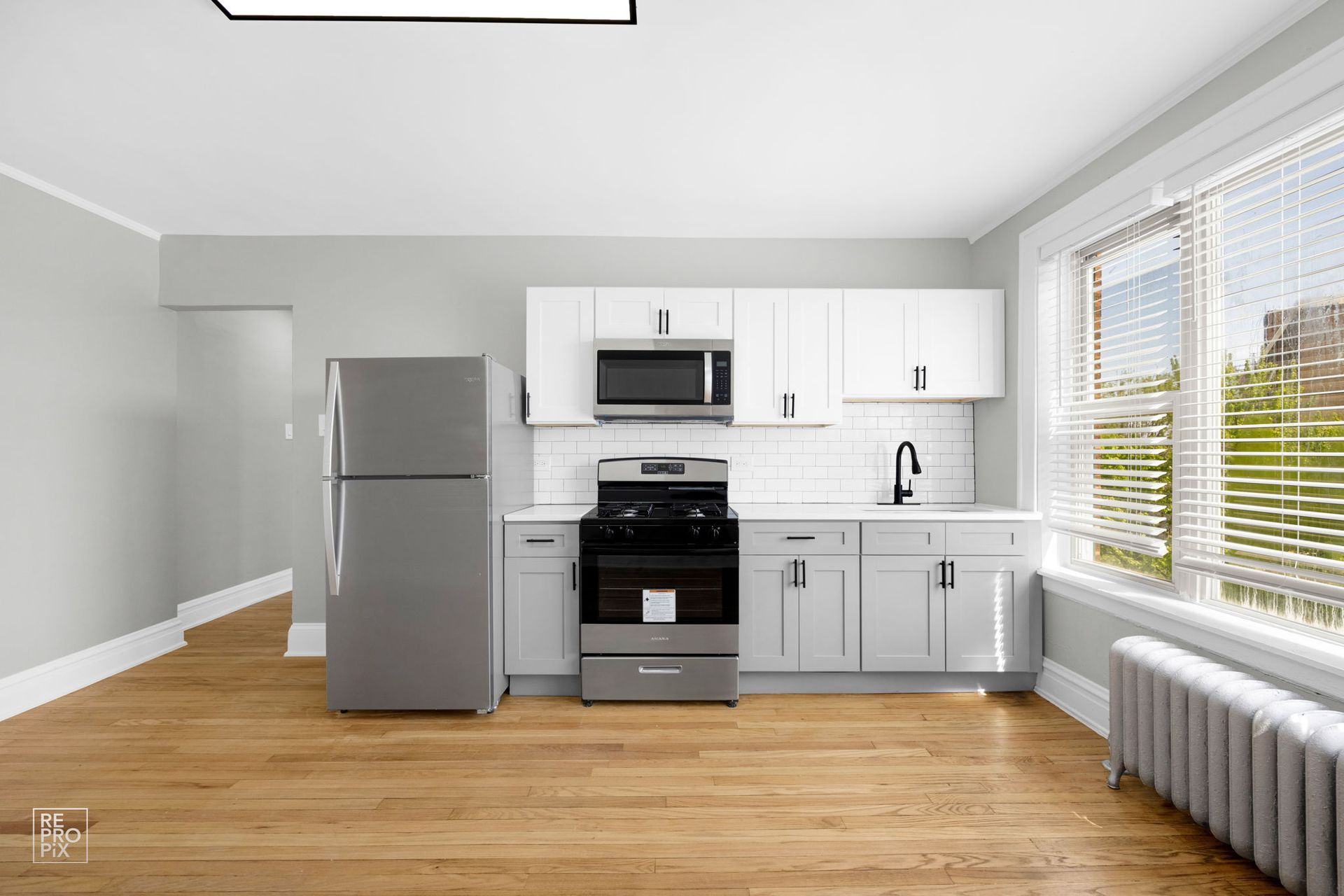 A bright, modern kitchen with white cabinets, stainless steel appliances, and a large window.
