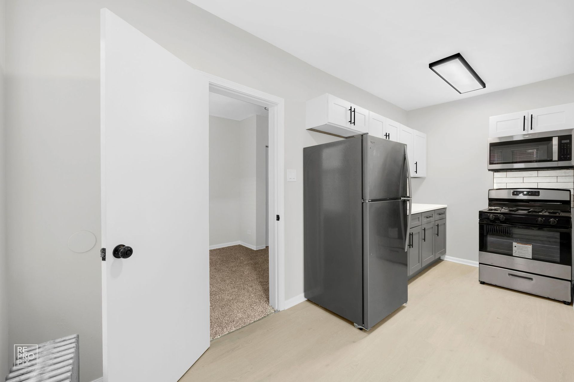 Kitchen with white cabinets, gray appliances, and an open doorway.