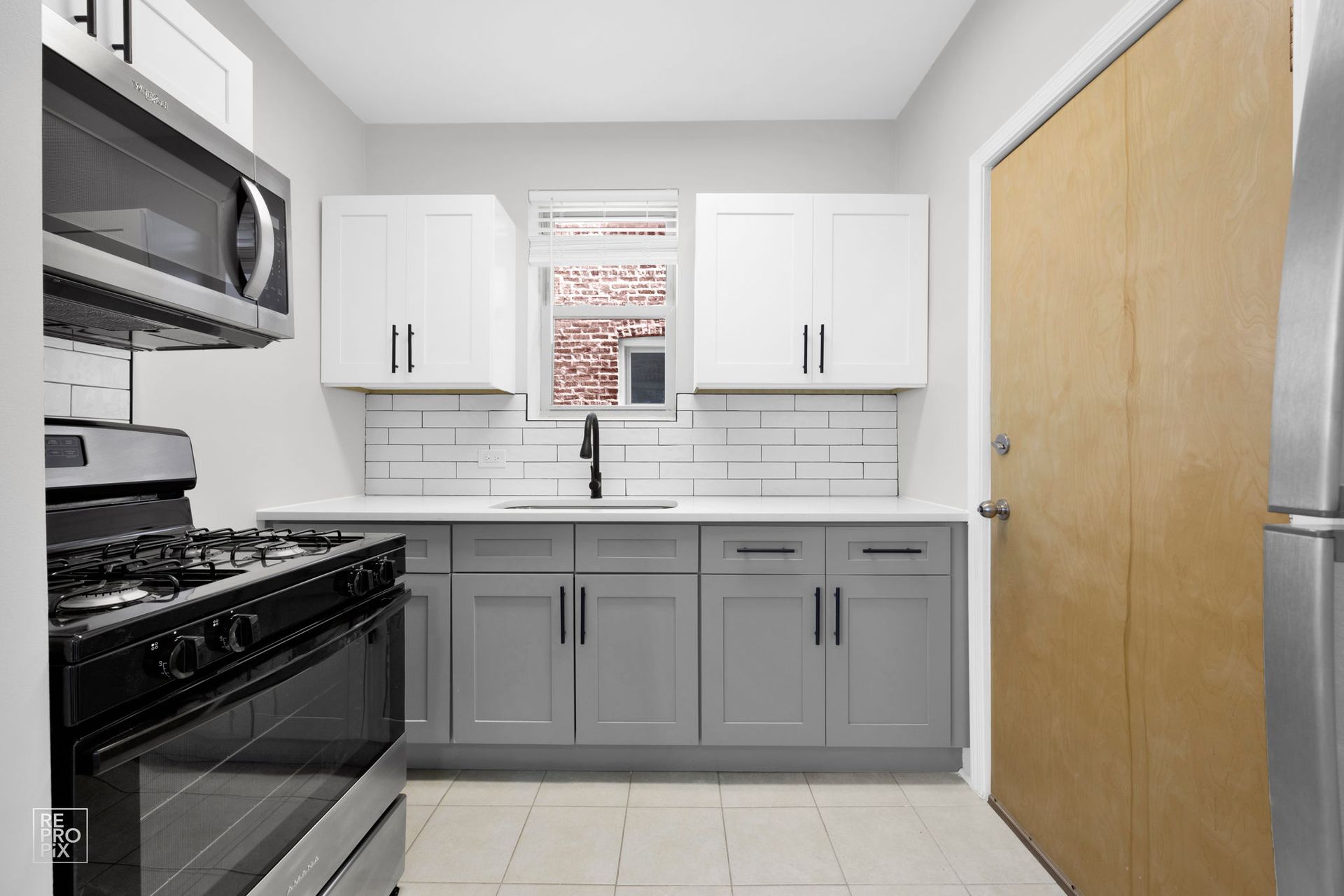 Kitchen with white and gray cabinets, stainless steel appliances, and a wood door.