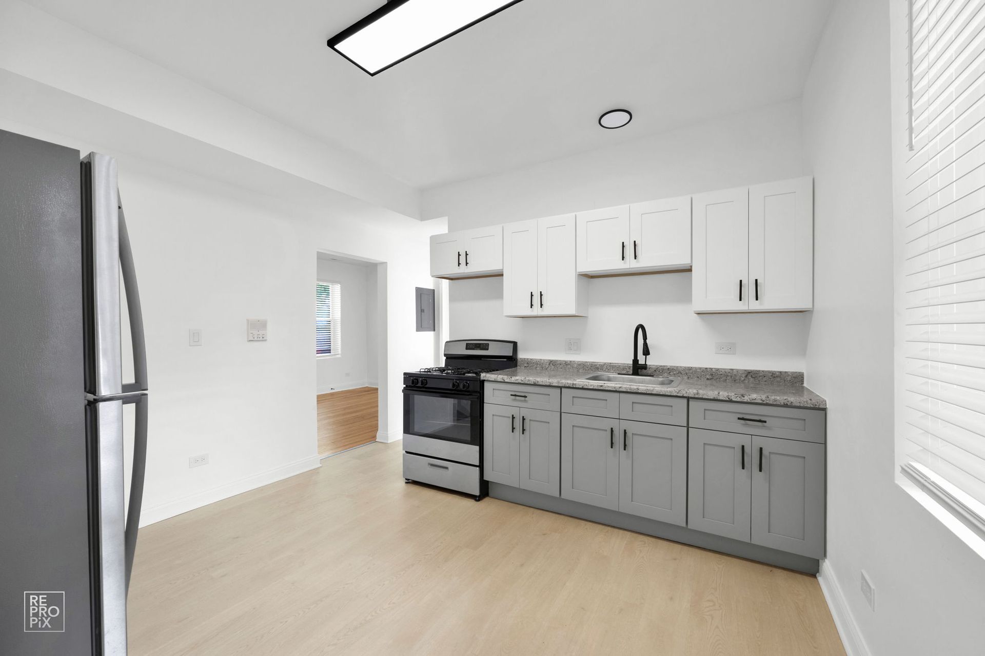 Kitchen with gray and white cabinets, stove, refrigerator, and light wood flooring.