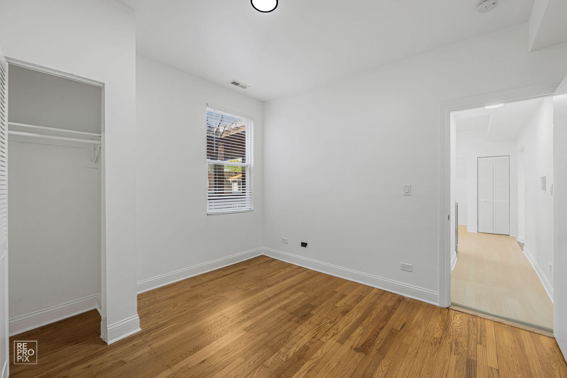 Empty room with hardwood floors, closet, window, and doorway to another room.