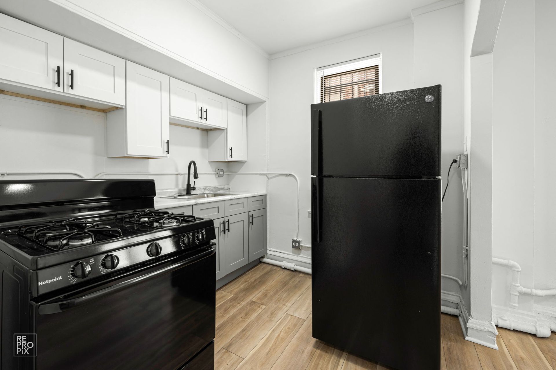 Black kitchen appliances in a kitchen with white cabinets, light gray counters, and wood-look floors.